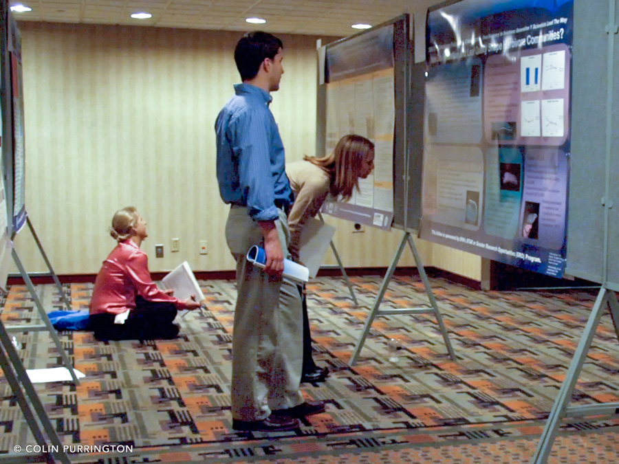 Viewers stooping to read conference poster in dimly-lit room